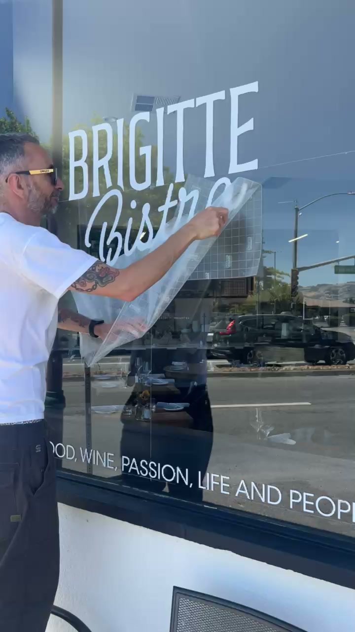 Peeling the transfer tape off the Brigitte Bistro logo decal on the front window