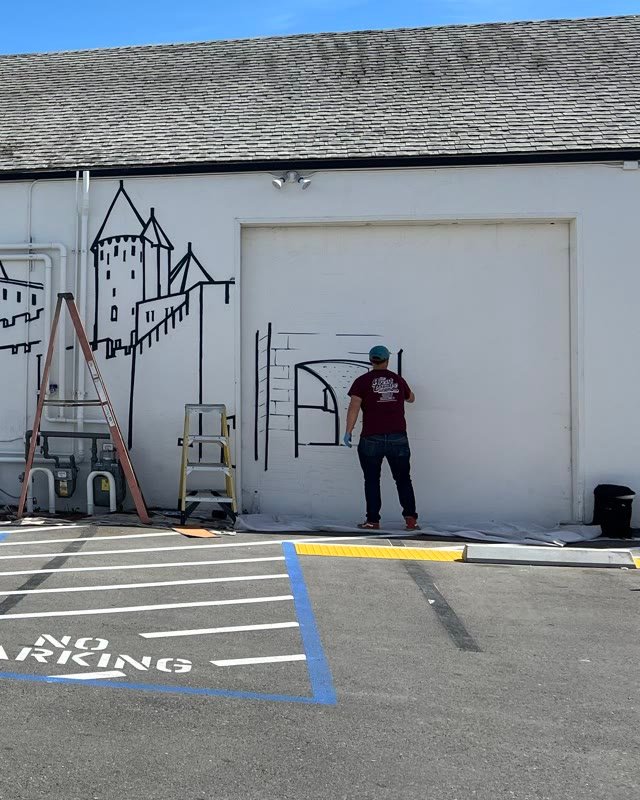 A muralist drawing the castle gate on the garage door in daylight