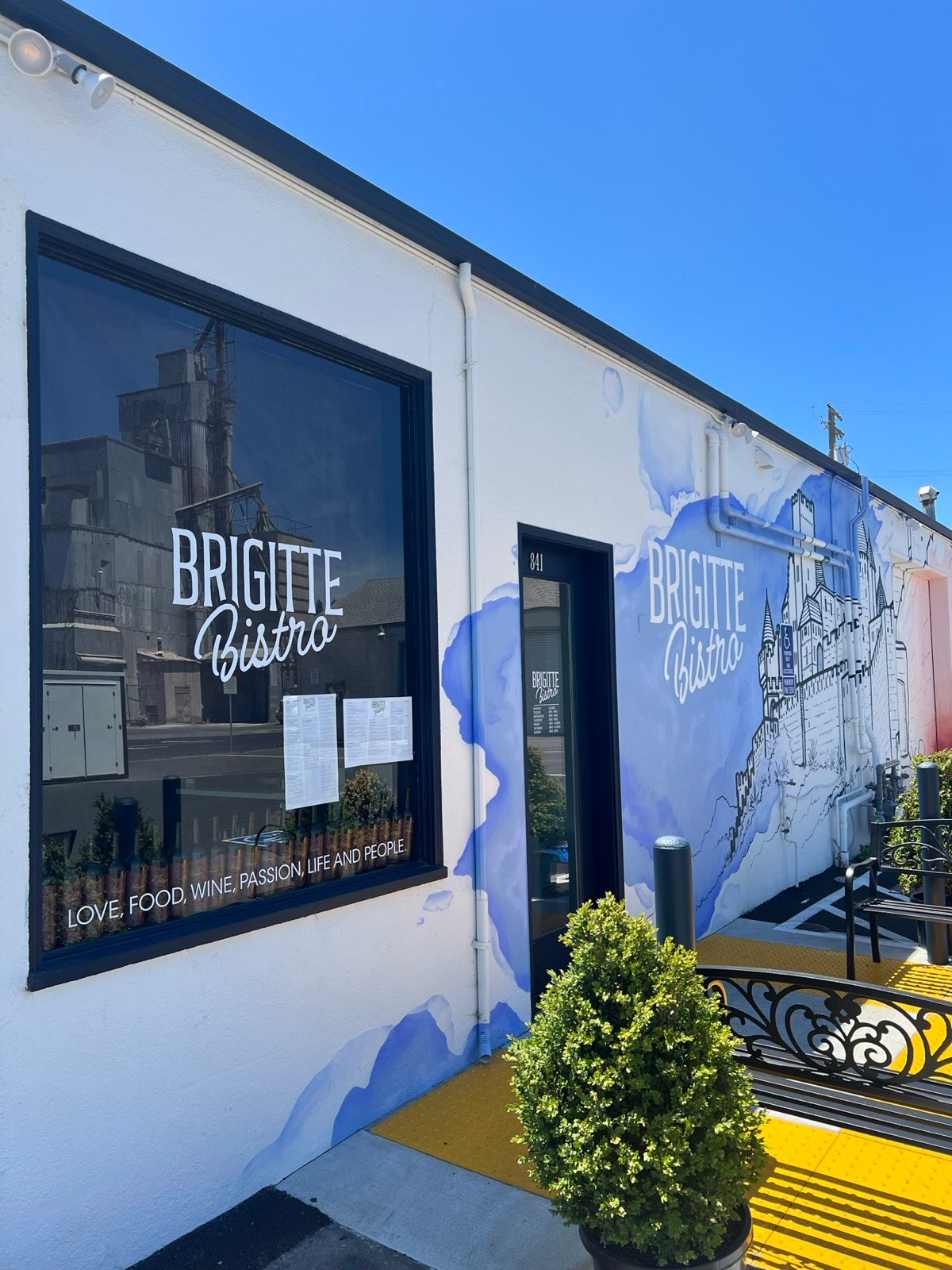 The Brigitte Bistro window with the logo decal and the house line, next to the mural