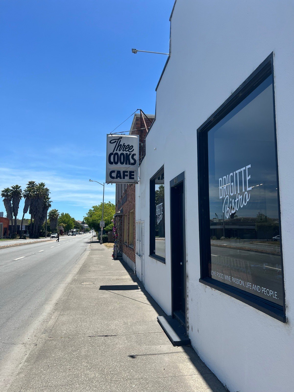 The Brigitte Bistro windows seen from the sidewalk, next to the Three Cooks Cafe sign